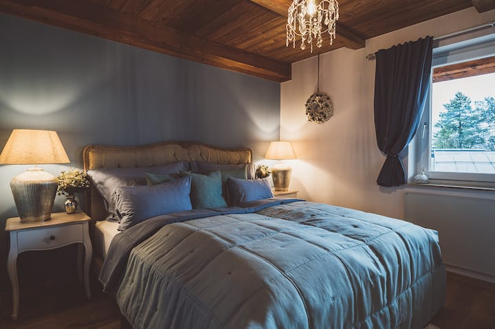 ห้องนอนที่มีสไตล์พร้อมเตียงคู่ที่นุ่มนวล แสงสว่างส่วนตัว และเพดานไม้ สีสันที่อบอุ่น วิวต้นไม้เขียวชอุ่มจากหน้าต่าง โต๊ะข้างเตียงที่หรูหรา และองค์ประกอบตกแต่งชวนให้คุณผ่อนคลาย เหมาะสำหรับการพักผ่อน