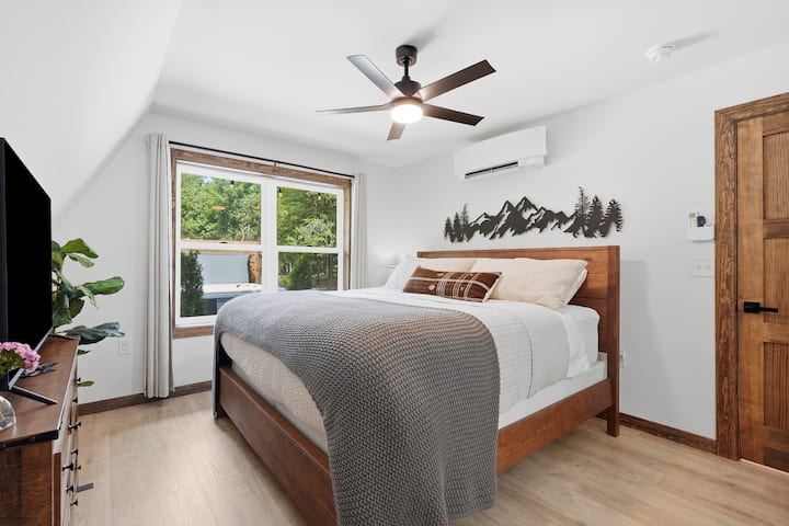 Dormitorio luminoso y acogedor con detalles en madera, TV, aire acondicionado y vistas tranquilas al bosque