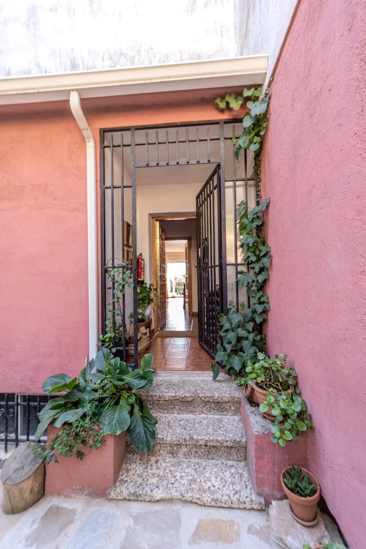 Entrada con carácter: fachada rosa, vegetación propia y acceso privado que te da la bienvenida desde el primer paso.