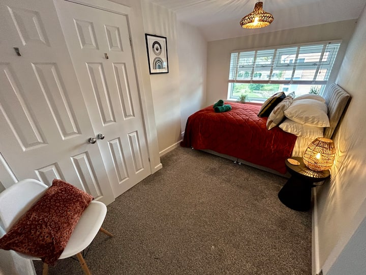 Двокреветна спална соба на првиот кат со поглед напред, со декор во неутрални меки кафеави тонови. Гардероба и стол. Поглед кон предната градина.