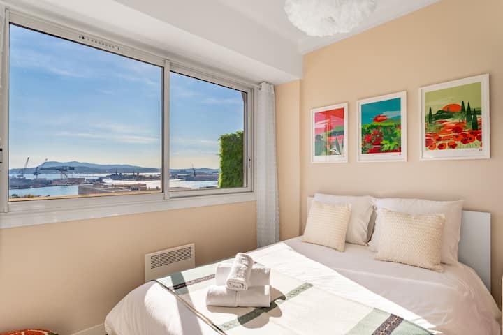 استيقظ مع البحر عند قدميك: ملاءات خفيفة ومناشف جاهزة وثلاث لوحات ملونة لمرافقة ضوء الصباح الذي يغمر الغرفة والميناء على بُعد.