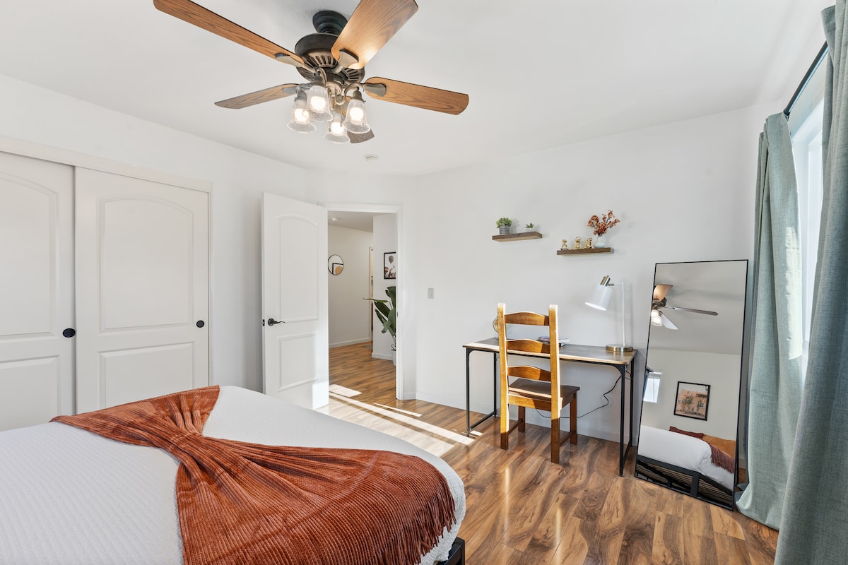 Гостинска спална соба со светли прозорци и удобен мебел.