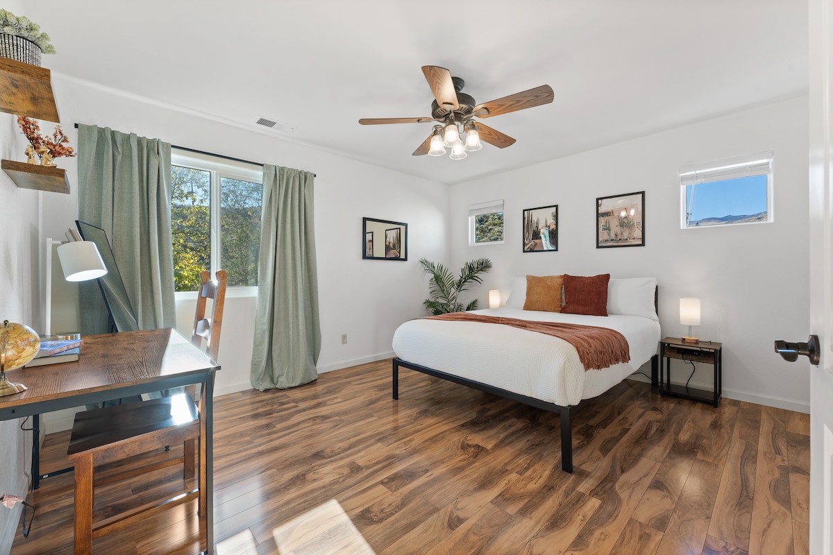 Гостинска спална соба со светли прозорци и удобен мебел.