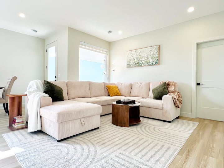 Dhomë ndenjjeje e ndritshme dhe mikpritëse me një divan seksional modern, thekse elegante dhe dritë të butë natyrale. Vendi i përkryer për t 'u çlodhur, për të lexuar ose për t' u mbledhur për një mbrëmje të qetë.