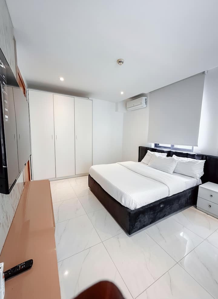 Moderna luksuzna spavaća soba s crnim baršunastim krevetom, mramornim podovima i bijelim ormarima.