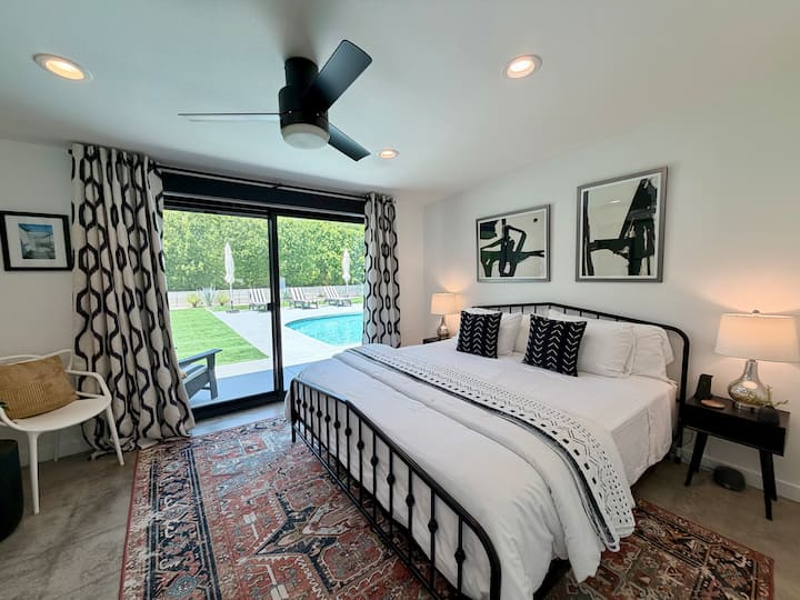 This modern bedroom pairs clean lines with a striking iron bed frame, bold black-and-white artwork, and a vintage rug layered over polished concrete floors. Slide open the glass doors and you’re steps from the pool and spa.