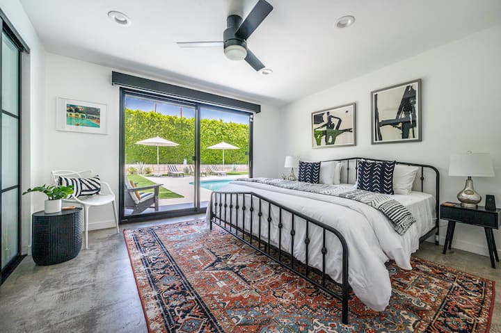 This modern bedroom pairs clean lines with a striking iron bed frame, bold black-and-white artwork, and a vintage rug layered over polished concrete floors. Slide open the glass doors and you’re steps from the pool and spa. 