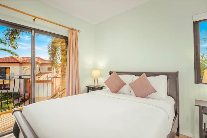 Útulná posteľ v červených tónoch a tropický výhľad cez široké okná vytvárajú teplé a pokojné ráno.