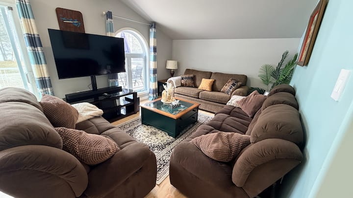 Open-concept living space featuring recliner sofas, large windows, and a 55” smart TV for movie nights.