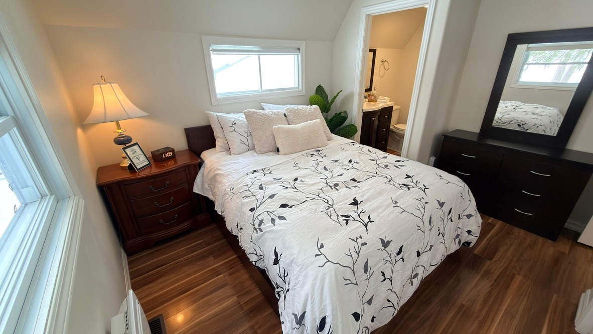 Comfortable queen bedroom with dresser, warm lighting, and convenient access to the ensuite bathroom.