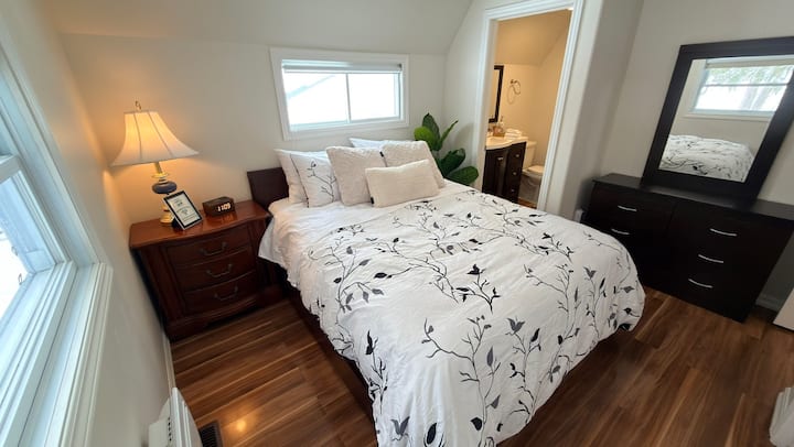Comfortable queen bedroom with dresser, warm lighting, and convenient access to the ensuite bathroom.