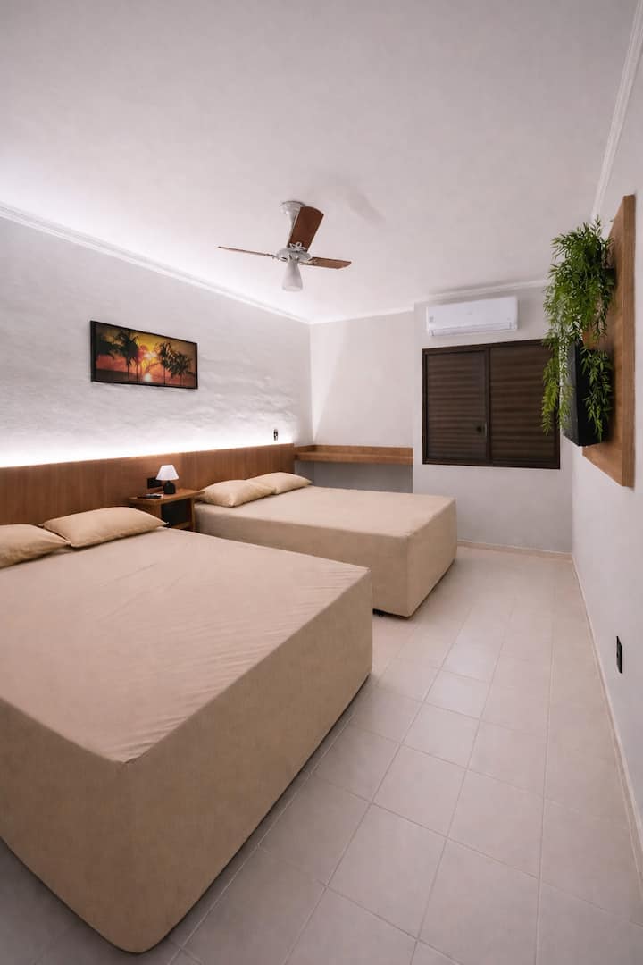 Chambre spacieuse avec deux lits doubles à sommier, télévision, climatisation et ventilateur de plafond.