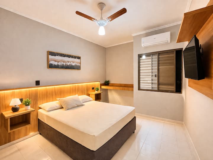 Chambre spacieuse avec un lit double à sommier, la climatisation, un ventilateur au plafond et une télévision.
