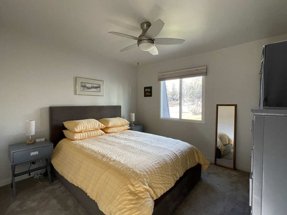 Dormitorio tranquilo y bien proporcionado con una cama tamaño queen, mesitas de noche dobles con acceso conveniente a la energía y muebles sencillos diseñados para el descanso y la comodidad.