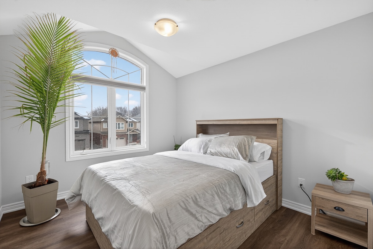 Светла спална соба со големи прозорци, совршена за рано будење. Удобниот кревет вклучува вграден простор за складирање за дополнителна практичност. Едноставниот декор, природната светлина и високата собна билка создаваат свеж, привлечен простор.