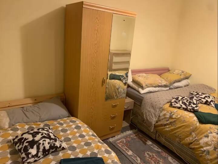 غرفة نوم مشرقة ومريحة تضم سريرين مفردين، مثالية للأصدقاء أو أفراد العائلة الذين يتشاركون المسكن، مع ديكور بسيط وأجواء مريحة.
