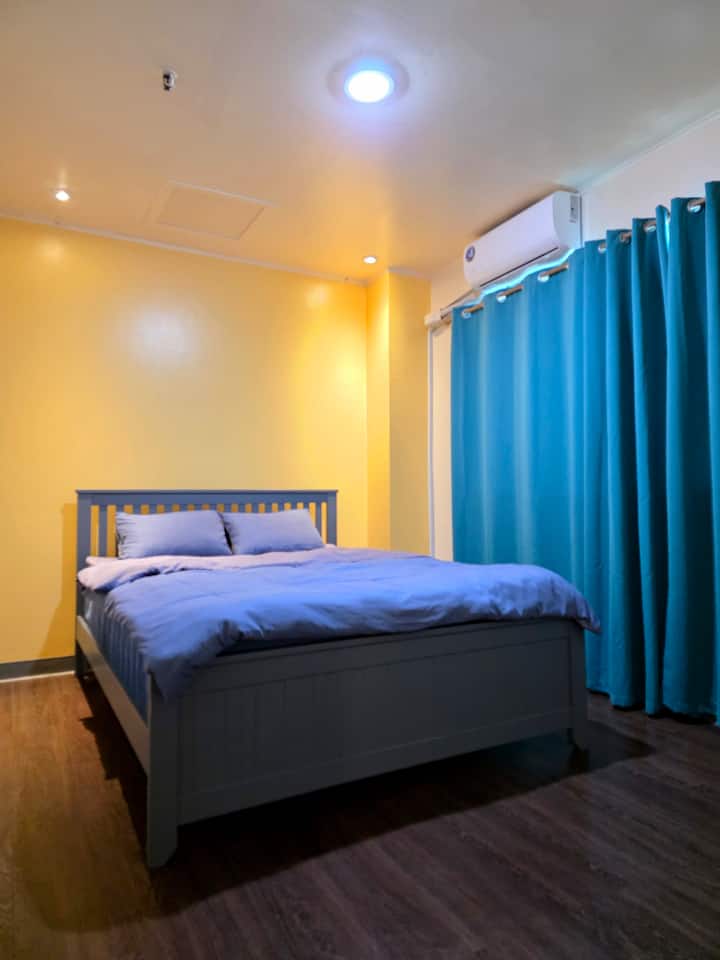 Bedroom includes a window for natural light, air conditioning for comfort, and a small hanger rack for your essentials (Queen Bed)