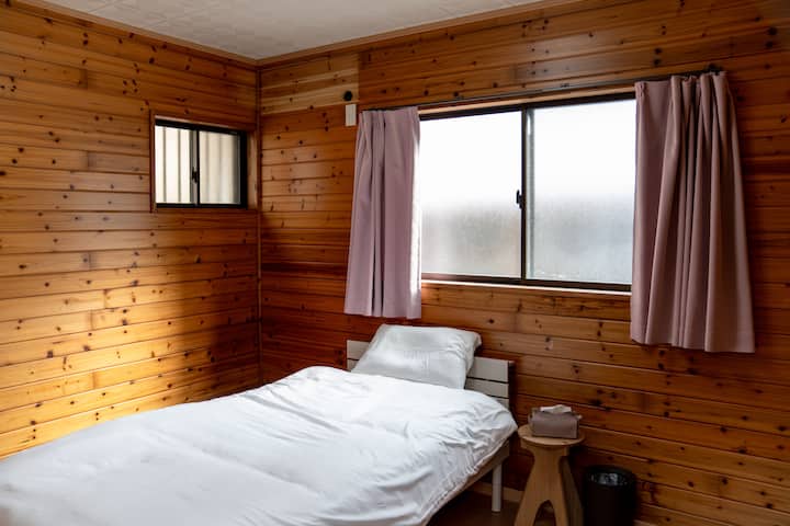 Es el dormitorio en el edificio separado (izquierda).Esta habitación tiene cortinas de color rosa ahumado y una cama individual blanca.