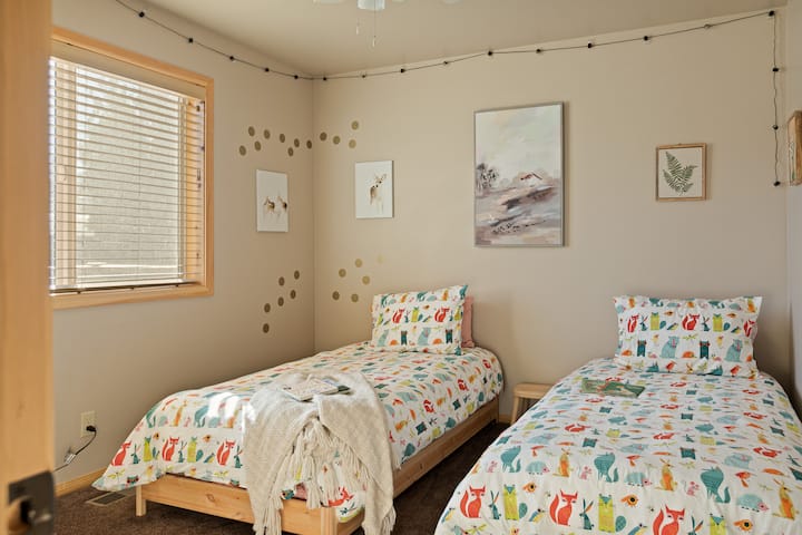 Svetlá spálňa s dvoma oddelenými posteľami, veselou posteľnou bielizňou a množstvom prirodzeného svetla.