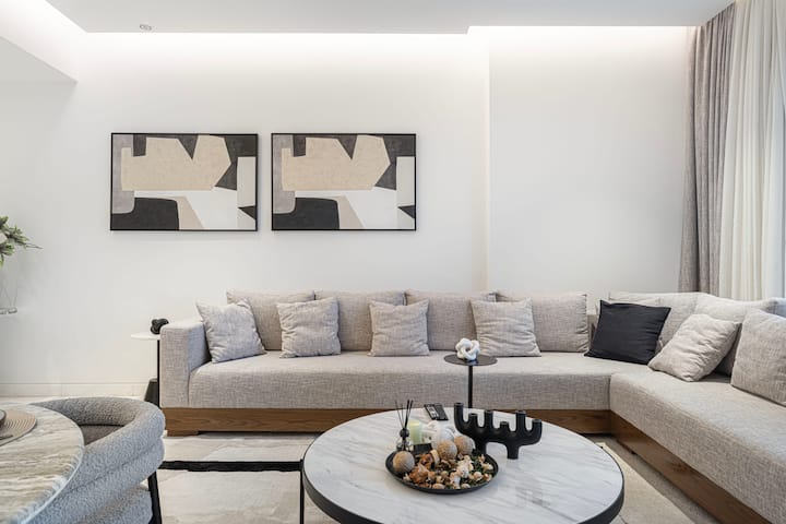 Enjoy a comfortable setting with a spacious L-shaped sofa, round coffee table, and modern wall art. Settle in for a quiet read, a chat, or a peaceful evening surrounded by the calm and inviting atmosphere of the living space.