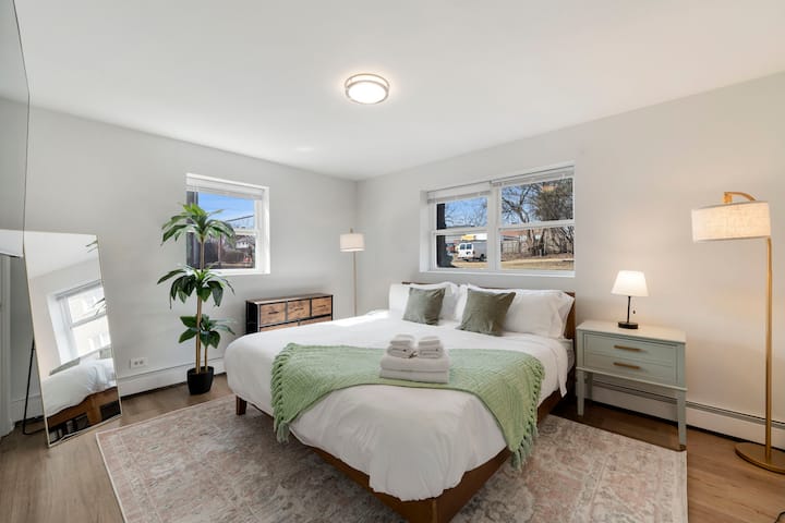 Një dhomë gjumi e bollshme me një krevat dopio "king", tavolinë pranë krevatit, pasqyrë të madhe, abazhur, dollap magazinimi dhe një impiant të rremë