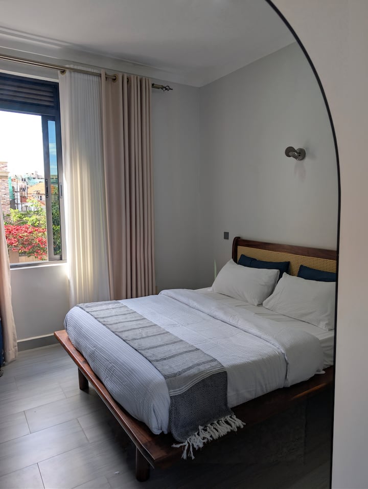 Ubytujte sa v štýlovom priestore! Posteľ s ratanovým povrchom, čerstvou posteľnou bielizňou a útulnou bielou prikrývkou sľubuje pokojný spánok. Zatemňovacie závesy zabezpečujú súkromie a hlboký odpočinok, zatiaľ čo okno ponúka krásny výhľad na farebnú záhradu.