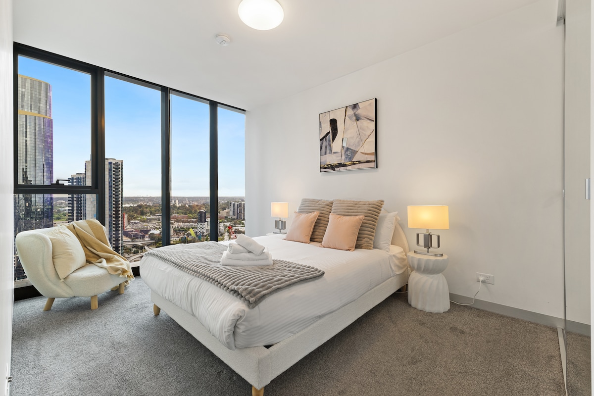 Hoofdslaapkamer met pluche beddengoed en uitzicht op de stad.