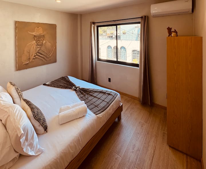 Situata all'ultimo piano, questa camera da letto matrimoniale è dotata di bagno privato, aria condizionata, armadio e una bella luce naturale e vista parziale sullo skyline di Reforma.
