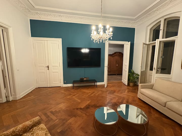 Sala de estar con un televisor muy grande de 80 pulgadas (aprox. 203 cm de diagonal de pantalla) y paso al dormitorio: una combinación de lo moderno y lo clásico.