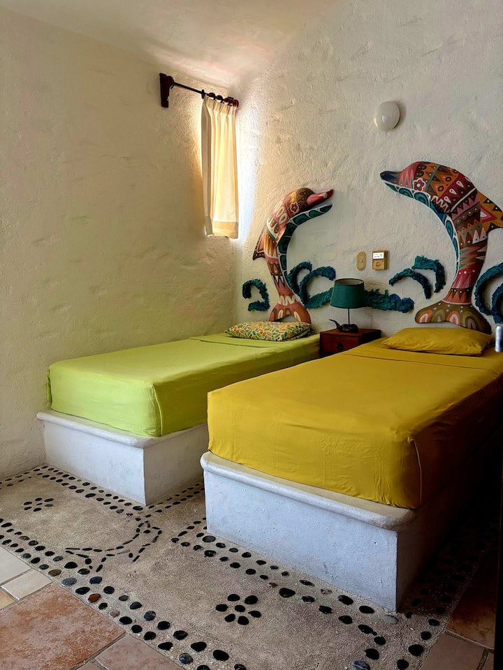Chambre 2
2 lits simples
Ventilateur de plafond
Climatisation
Placard
Petit patio sur le côté qui communique avec le 2e salon
L'art derrière le lit peint par un artiste local à Huatulco