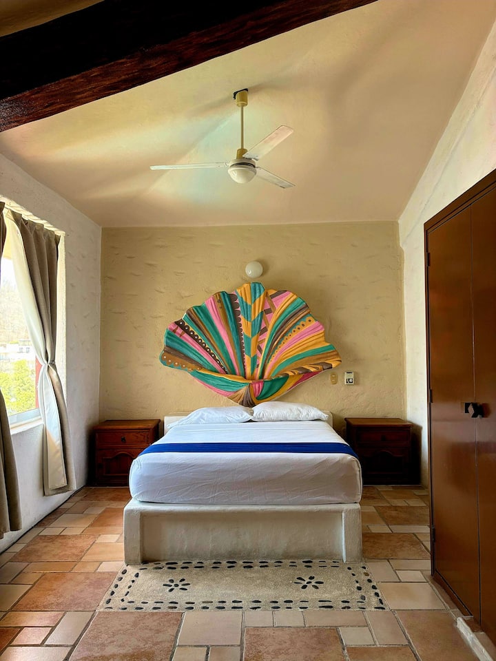 Chambre principale
- Lit queen size
- Ventilateur de plafond
- Climatisation
-Closet
- Télévision intelligente
- Salle de bain attenante
- Coin salon ;
- Grandes fenêtres avec lumière naturelle

Art derrière le lit, peint par un artiste local à Huatulco