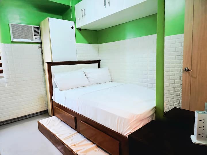 Full-size Bed with a single bed pull-out and drawers, Panasonic Window Aircon with NanoEx technology, wardrobe cabinet, charging station with surge protector, Vanity Mirror, Table with drawers