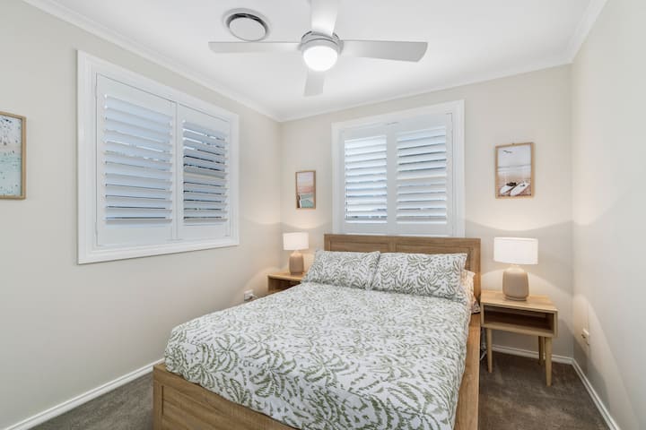 Rest easy in the second queen bedroom, where quality beddings, a ceiling fan, and soft natural light combine to create a calm, restful retreat.