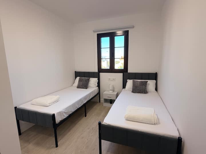 Dormitorio secundario con dos camas individuales de 90. Almohadas cómodas y cojines extras, se incluye ropa de cama extra. Una mesita de noche con una pequeña luz y dos enchufes.