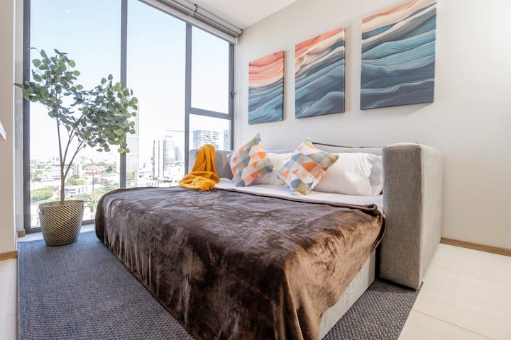 Sala luminosa y moderna con amplios ventanales que ofrecen una vista espectacular de la ciudad. Equipada con un cómodo sofá cama, aire acondicionado y TV, este espacio combina confort y estilo, ideal para relajarte