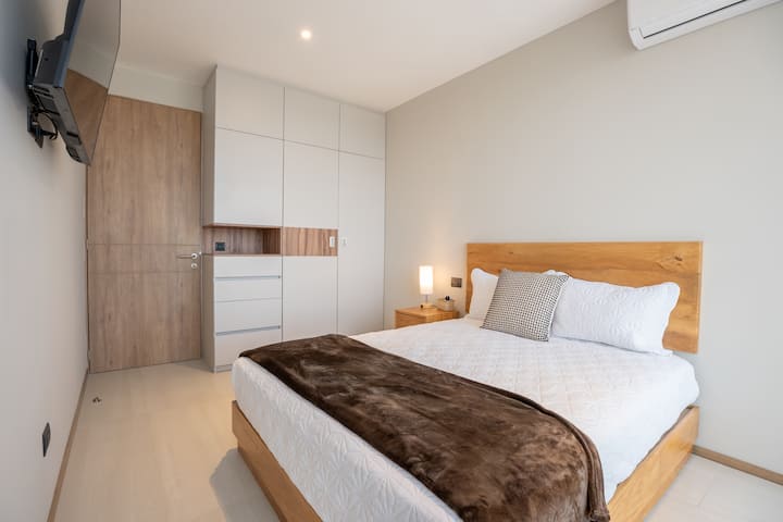Habitación con cama queen, aire acondicionado, TV y acceso a un balcón privado. Su decoración moderna y ambiente tranquilo ofrecen el lugar perfecto para un descanso.