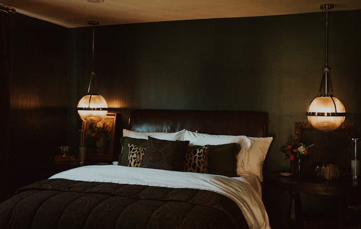 A queen bed anchors the room, with layered bedding and a selection of pillows, including ergonomic, body, and standard options, to suit individual comfort preferences.