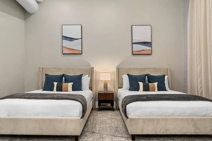 ห้องนอนสว่างด้วยเตียงควีนไซส์ 2 เตียง งานศิลปะที่เข้ากัน และเครื่องนอนหลายชั้นที่อบอุ่น เหมาะสำหรับครอบครัวหรือกลุ่ม