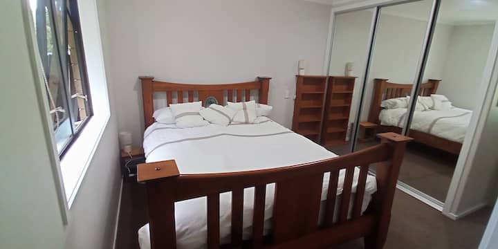 Photo mise à jour de la chambre principale avec salle de bain attenante, montrant le nouveau lit, magnifiquement fabriqué à partir de bois massif recyclé Rimu avec un vitrail. (Décembre 2025)