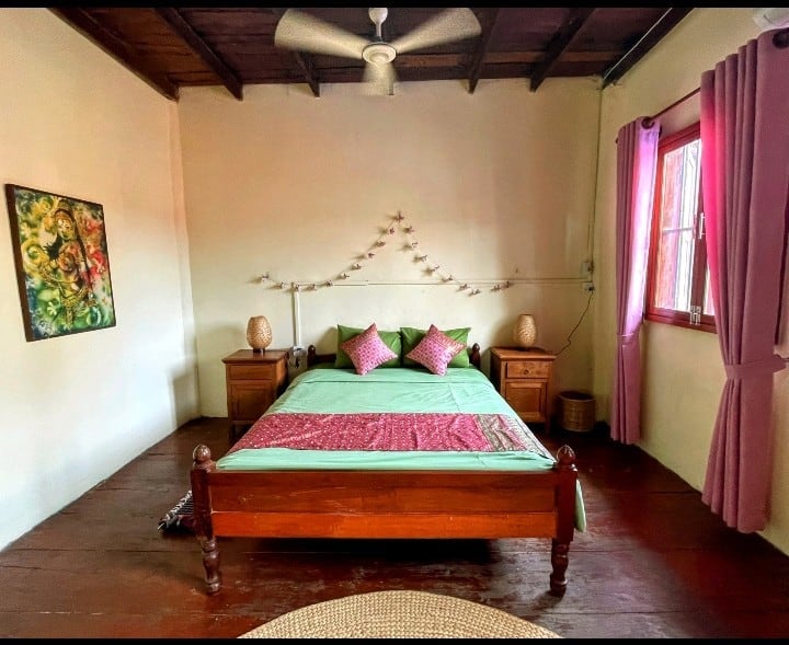 Master bedroom from the foot of the bed – queen-size teak four-poster, soft lotus farm inspired linens, original dark-wood floors, and a ceiling fan that keeps everything perfectly cool. Simple, spacious, and made for the deepest Kampot sleep. ️✨