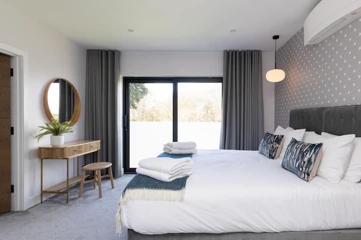 Bright and stylish bedroom featuring a comfortable bed, air conditioning, dressing table and large sliding glass doors, allowing plenty of natural light into the room.