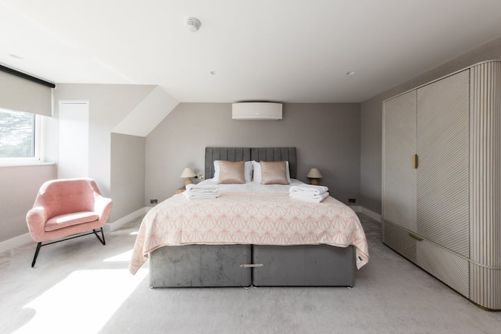 Bright and spacious bedroom with a super king-size bed, bespoke fitted wardrobe, soft neutral décor, plush carpeting, and large window providing excellent natural light and a calm, contemporary feel.