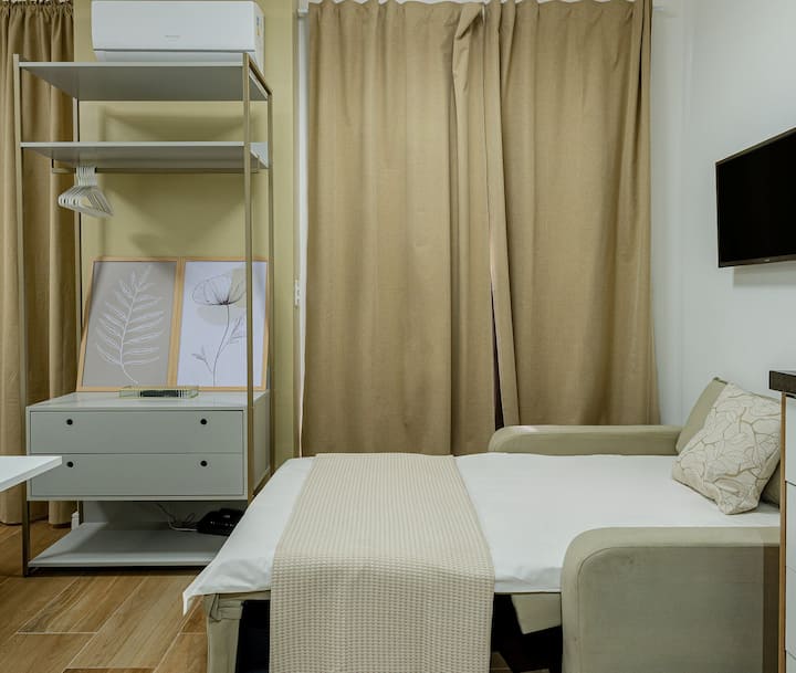 ห้องนั่งเล่นรวมกับห้องนอนและห้องครัวในสภาพแวดล้อมที่ใช้งานได้จริงและอบอุ่น มีเตียงโซฟา เครื่องปรับอากาศ สมาร์ททีวี ผ้าม่านบล็อกแสง และทางออกตรงไปยังระเบียง