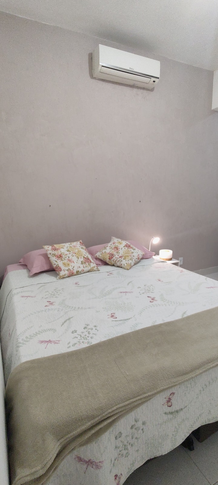 Cama tamaño queen con mesita de noche con luz de lectura y router Wi-Fi al lado de la cama.