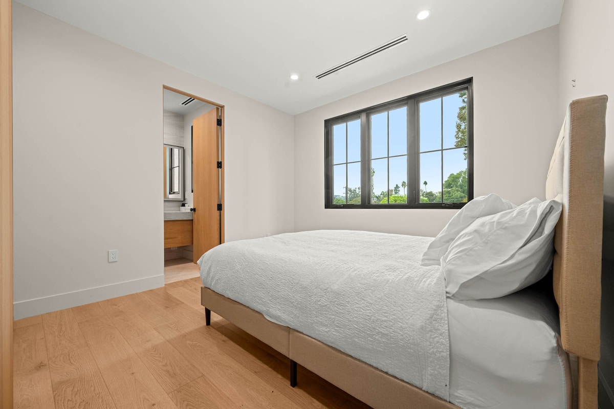 Dormitorio 2 con cama tamaño queen (capacidad para 2 personas). Cuenta con una gran ventana, pisos de madera y acceso directo a un baño privado.