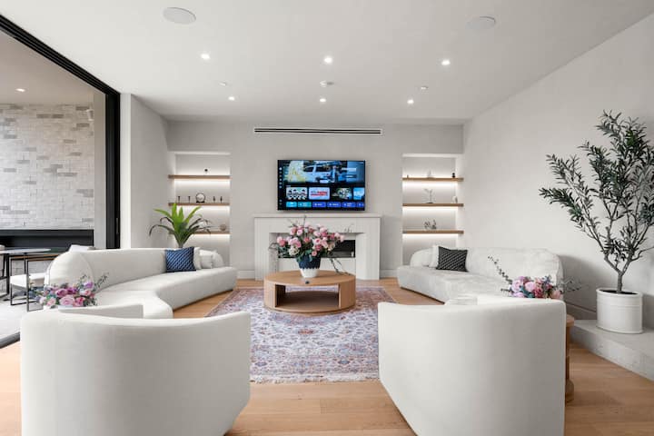 Dhomë ndenjjeje e ndriçuar, me koncept të hapur, me oxhak, televizor të montuar dhe qasje pa ndërprerje nga brenda dhe jashtë në oborrin privat.