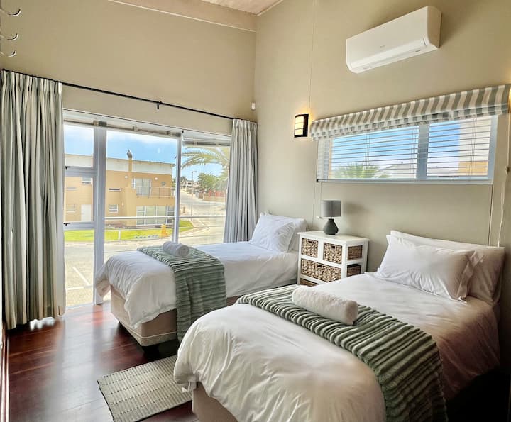 Habitación doble llena de luz con aire acondicionado y ropa de cama de primera calidad, que ofrece una estancia cómoda y elegante en este lujoso alojamiento ejecutivo frente a la playa de Swakopmund.