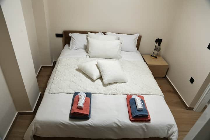 Cama doble con ropa de cama blanca limpia, almohadas adicionales y toallas dispuestas, ideal para parejas o viajeros solos en Kallithea.