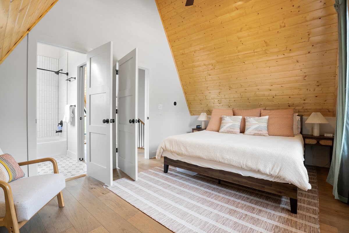 غرفة نوم في الطابق العلوي بسرير كينج وحمام داخلي.  شاحن هاتف لاسلكي على جانب واحد من السرير وشريط طاقة مع منافذ USB على الجانب الآخر.