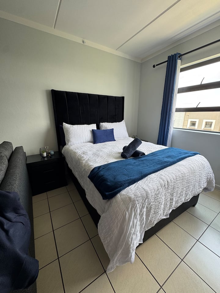 Bright and inviting studio featuring a neatly made double bed with crisp white linen and stylish navy accents. 
